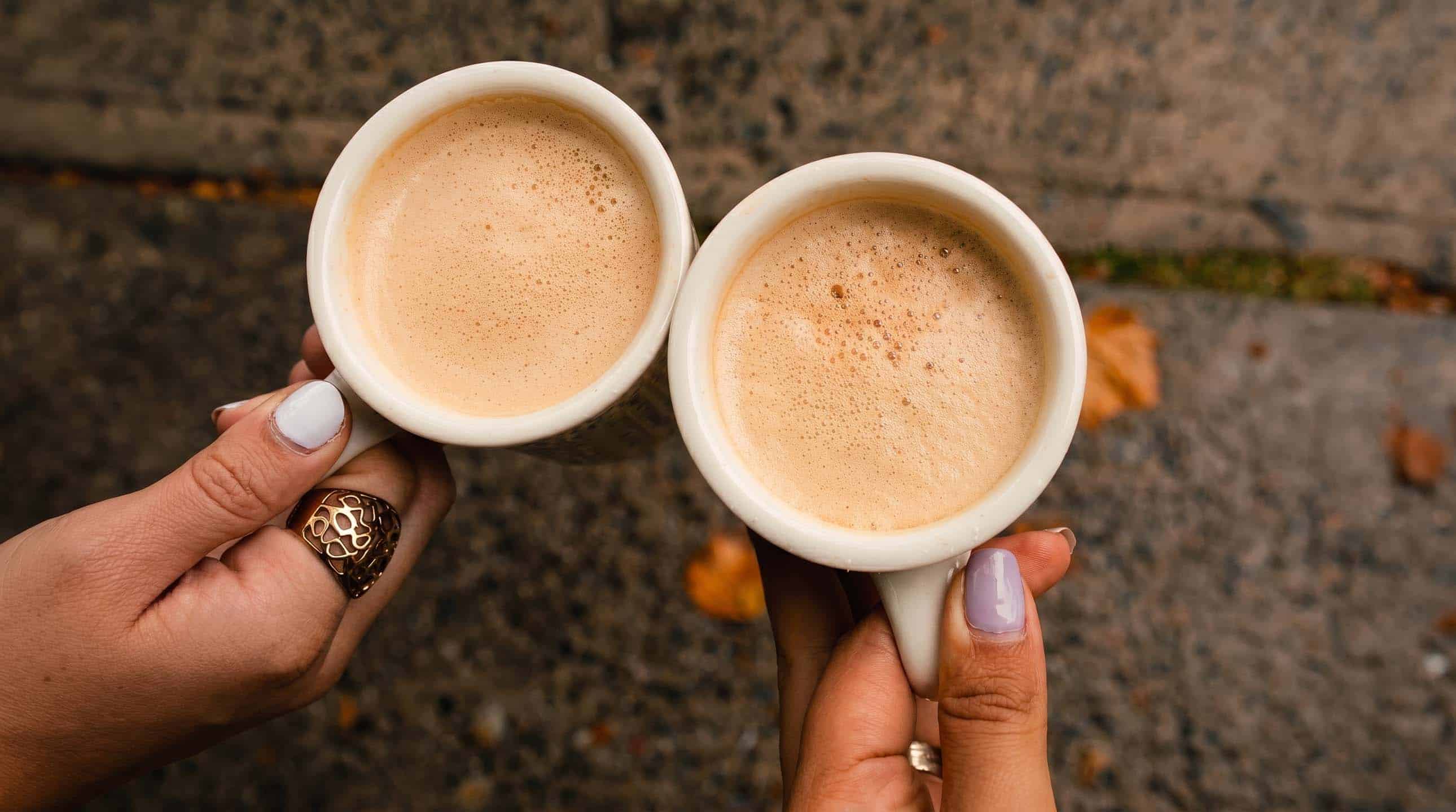 Two hands holding warm cups of fresh Venezuelan coffee outside the café.