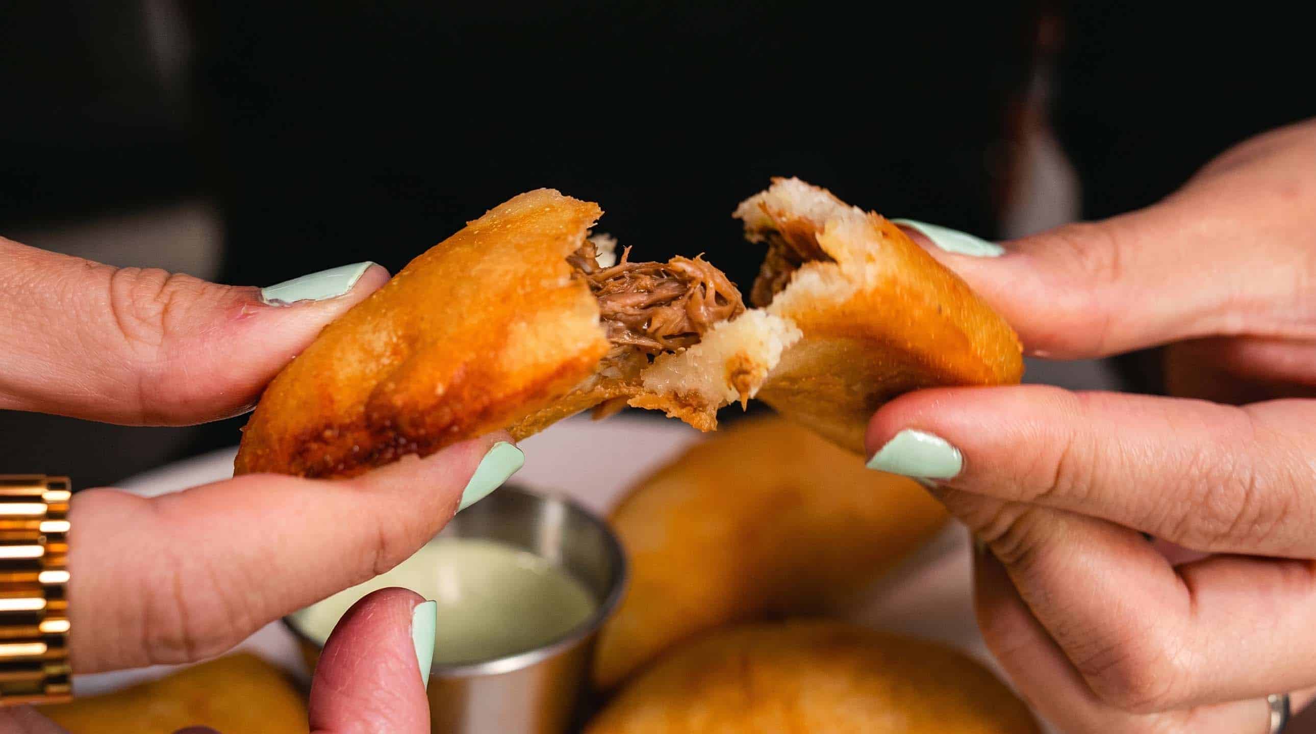 A hand-pulled Venezuelan empanada revealing tender shredded beef inside a crisp golden shell.