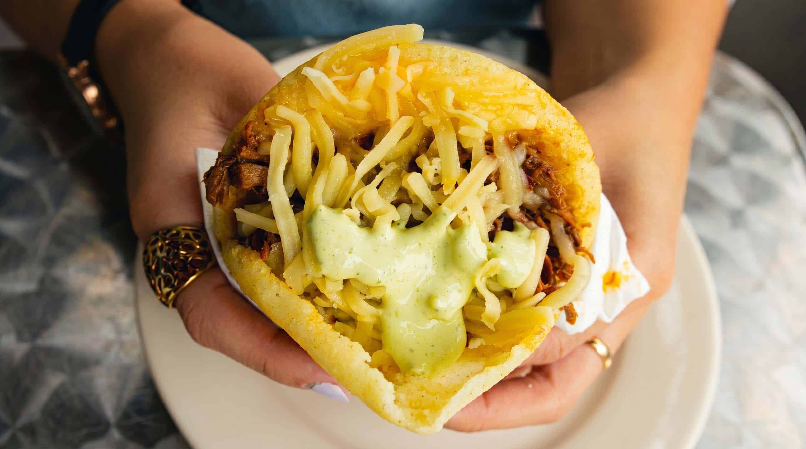 Golden arepa filled with shredded beef, white cheese, and creamy avocado-cilantro sauce.