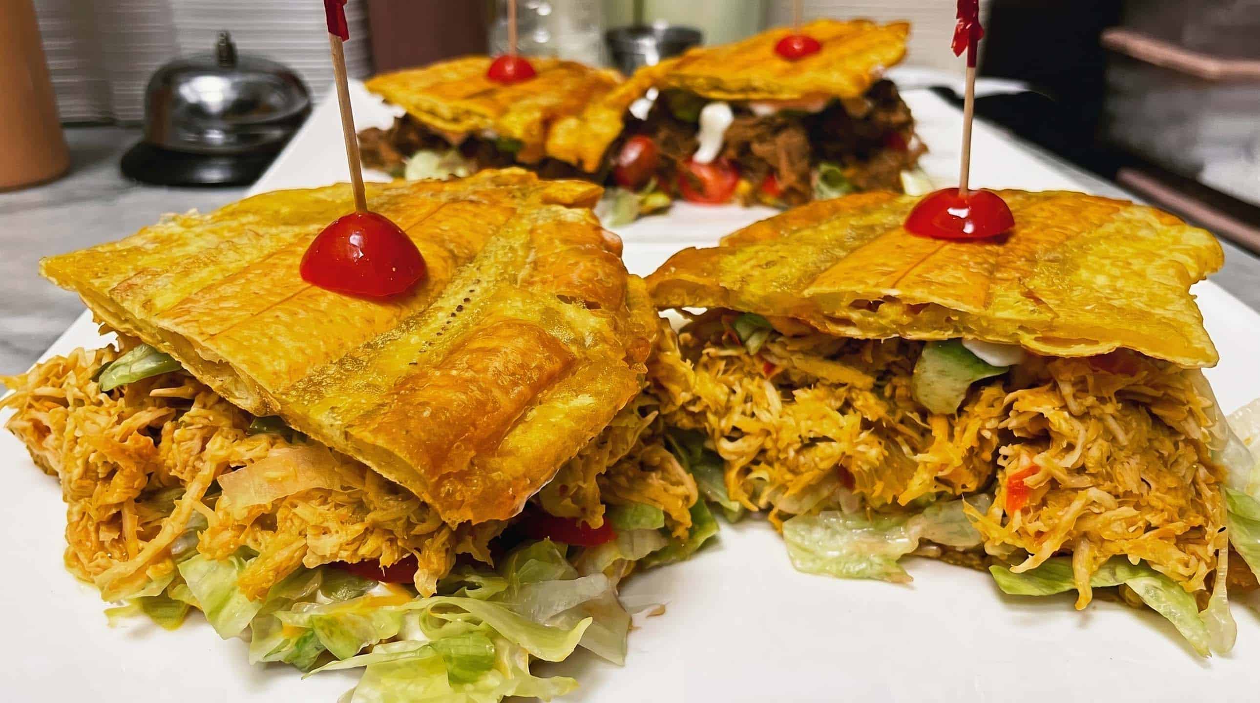 Crispy plantain patacón sandwiches stacked and topped with shredded chicken and lettuce.