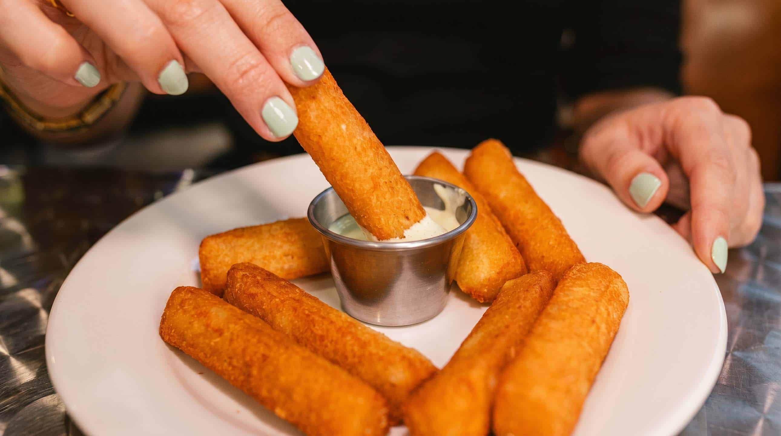 Plate of crispy Venezuelan tequeños with creamy garlic dipping sauce.